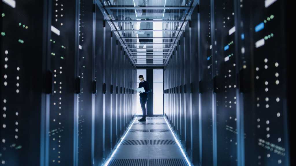 Male IT Engineer Works on a Laptop in a Big Data Center